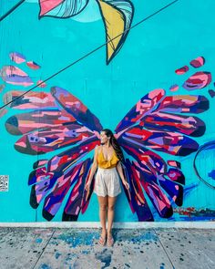 a woman standing in front of a colorful wall with a large butterfly painted on it