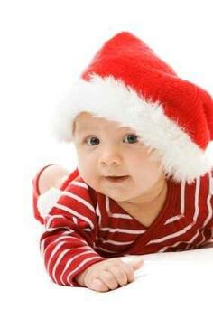 a baby wearing a santa hat laying on its stomach and looking up at the camera