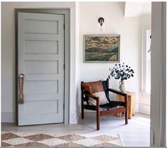 a chair sitting in front of a door with a vase on the floor next to it