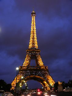 the eiffel tower lit up at night with cars passing by in front of it