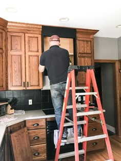 a man standing on a step ladder in a kitchen next to wooden cabinets and an oven