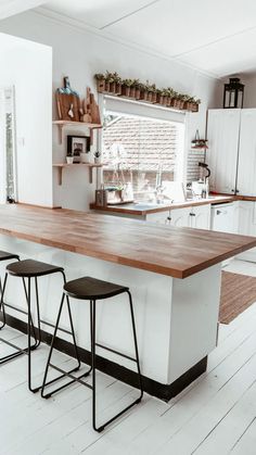 two stools are sitting at the counter in this white and wood kitchen with open shelving