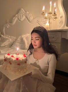 a woman holding a cake with candles on it in front of a bed and chandelier