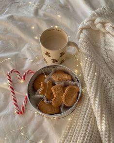 a cup of coffee next to some cookies and candy canes on a white blanket