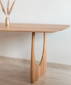 a wooden table sitting on top of a hard wood floor next to a vase filled with dry grass