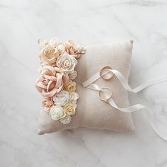 a ring pillow with flowers on it sitting on a white marble surface next to a ribbon