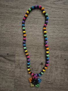 a multicolored beaded necklace is displayed on a wooden surface with a small flower