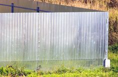 a large metal structure sitting in the middle of a field next to tall grass and trees