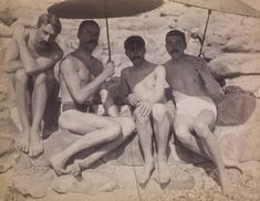 four men sitting under an umbrella on the beach