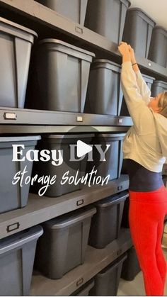 a woman in red pants and white shirt placing plastic bins on shelving unit