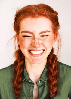 a woman with red hair and freckled eyes smiles while wearing a green shirt