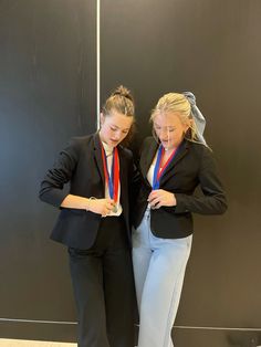 two women standing next to each other in front of a wall with medals on it