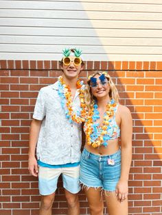 two people standing next to each other in front of a brick wall wearing leis