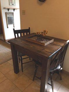 a wooden table with two chairs and a book on it in front of a clock