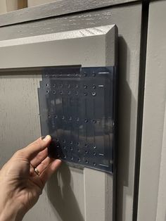 a person's hand is pressing the latch on a gray door with rivets