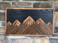 a wooden sign on a stone wall with mountains painted on it's back side