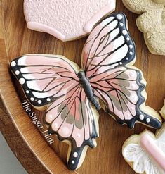 decorated cookies in the shape of butterflies on a wooden platter with pink and white frosting