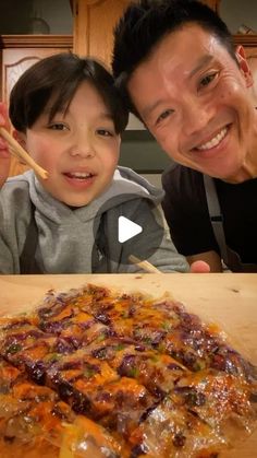 a man and boy are smiling at the camera while they eat pizza with chopsticks in front of them