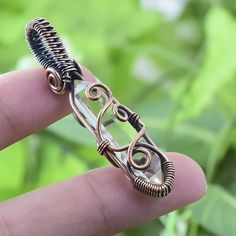 a wire wrapped ring sitting on top of a persons finger with green leaves in the background