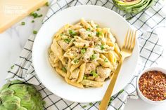 a white bowl filled with pasta next to an artichoke