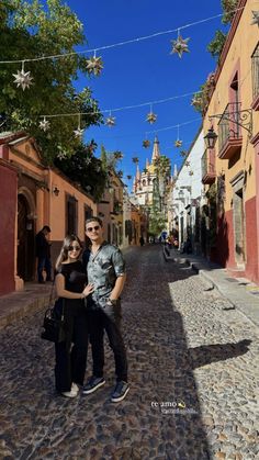 two people standing in the middle of a cobblestone street with star decorations hanging above them