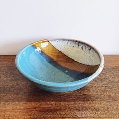 a blue and brown bowl sitting on top of a wooden table next to a white wall