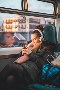 a woman sitting on a train looking at her cell phone while listening to headphones