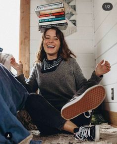 a woman is sitting on the floor with books stacked on her head and smiling at the camera