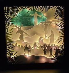 paper cut nativity scene displayed in dark room with green lights and palm tree leaves