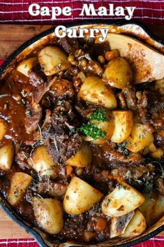 a bowl filled with meat and potatoes on top of a wooden table next to a red towel