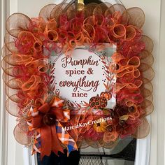 a pumpkin wreath with orange and red ribbons hanging on the front door to welcome guests