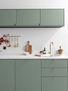 a kitchen with green cabinetry and white counter tops, gold faucets on the wall