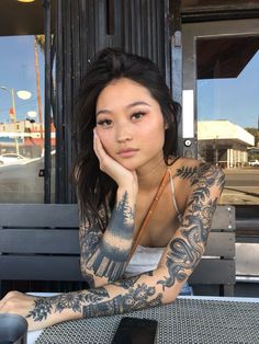 a woman sitting at a table with tattoos on her arm and arms behind her head