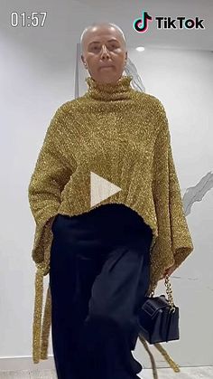 a woman in a gold sweater and black pants with a handbag on her hip