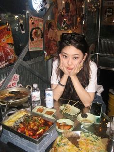 a woman sitting at a table with food in bowls and chopsticks on it