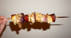 a person is holding up a skewer with meat wrapped in bacon on it