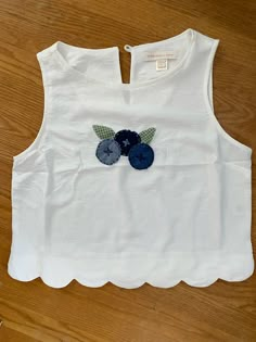 a white top with two blue flowers on the front and one green flower on the back