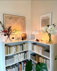 a white book shelf filled with lots of books next to a lamp and vase full of flowers