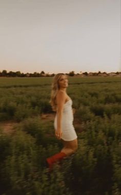 a woman in white dress and red boots walking through an open field