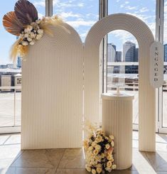 two white vases with flowers on them in front of large windows and cityscape