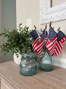 two mason jars with american flags in them are sitting on a counter next to a potted plant