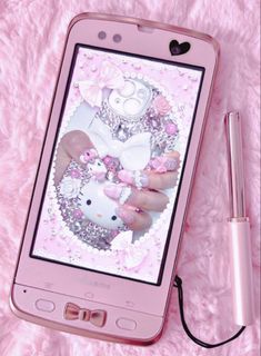 a pink cell phone with hello kitty on the screen and a pen next to it