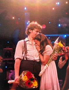 a man and woman standing next to each other in front of a crowd holding flowers