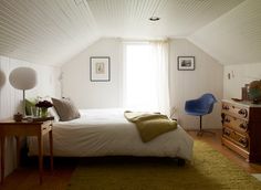 a bedroom with a bed, dresser and chair next to a window in the ceiling