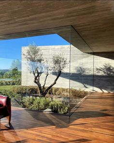 an empty chair in front of a glass wall with trees and bushes on the other side