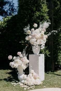 two white vases filled with flowers sitting on top of a grass covered park area