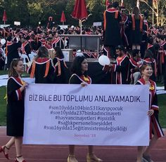 two women holding a banner in front of a large group of people wearing graduation gowns