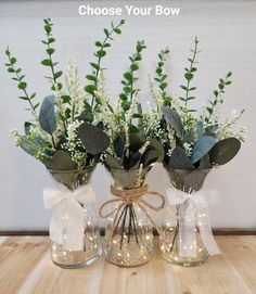 three glass vases with flowers and greenery in them on a wooden table top