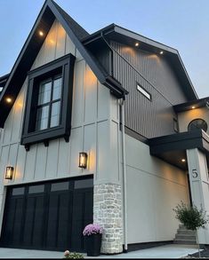 a large house with black shutters and lights on the front door is shown at dusk