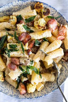 a pasta dish with bacon, spinach and cauliflower in a blue and white bowl